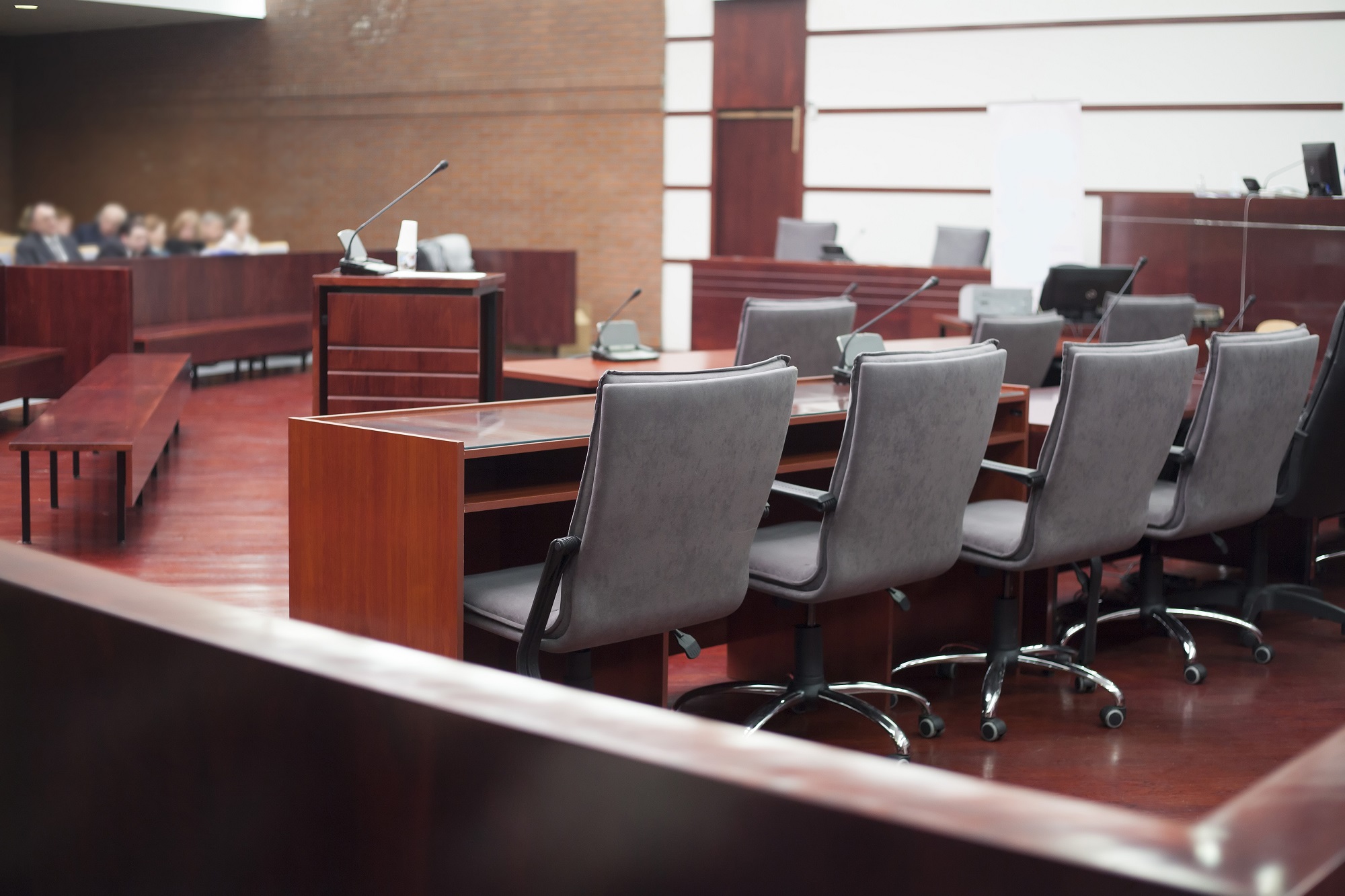 A stock photo of a mostly empty courtroom with some spectators in the background